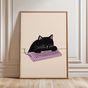 May include: Framed art print showing a black cat asleep on a pink computer keyboard. The cat has closed eyes and white whiskers. The artwork is set against a cream background and framed in a gold-coloured frame.