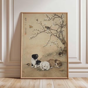 May include: A framed print of a Japanese-style illustration. The artwork shows puppies resting under a flowering tree with a bird and butterfly. The color palette includes beige, brown, black, white, and touches of red. The frame is wooden.