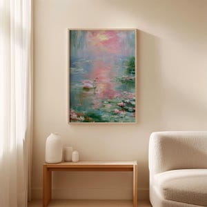 May include: A framed painting depicts a serene water scene with two white swans. The artwork features a soft color palette of pink, blue, and green, with visible brushstrokes. The painting is displayed above a wooden table.