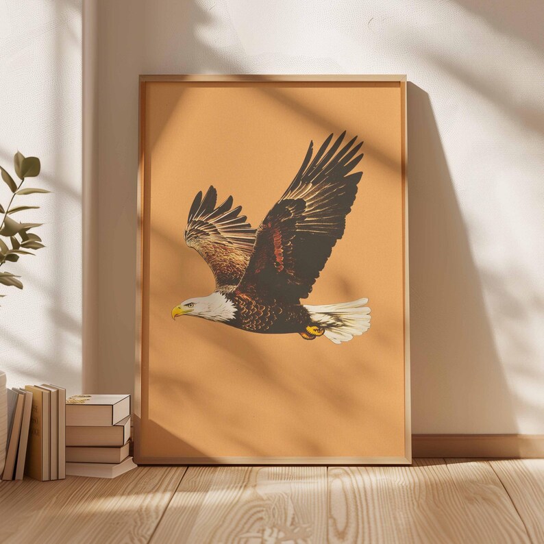 May include: Framed print featuring a bald eagle in flight. The eagle has brown and white feathers, a yellow beak, and a white head. The background is a solid orange color. The print is in a wooden frame.