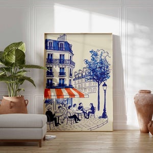 K&ouml;nnte beinhalten: Ein gerahmter Kunstdruck zeigt eine Pariser Caf&eacute;szene in blauer und wei&szlig;er Tinte. Das Kunstwerk zeigt ein Geb&auml;ude mit einer rot-wei&szlig; gestreiften Markise, einen Baum und Figuren, die an Tischen sitzen. Eine gro&szlig;e Topfpflanze, ein grauer Hocker und Terrakotta-Vasen befinden sich im Vordergrund.