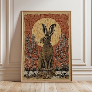 May include: Framed art print featuring a detailed illustration of a brown hare with long ears, set against a red and yellow background with a circular sun design. The artwork includes stylized plants and is displayed in a wooden frame.