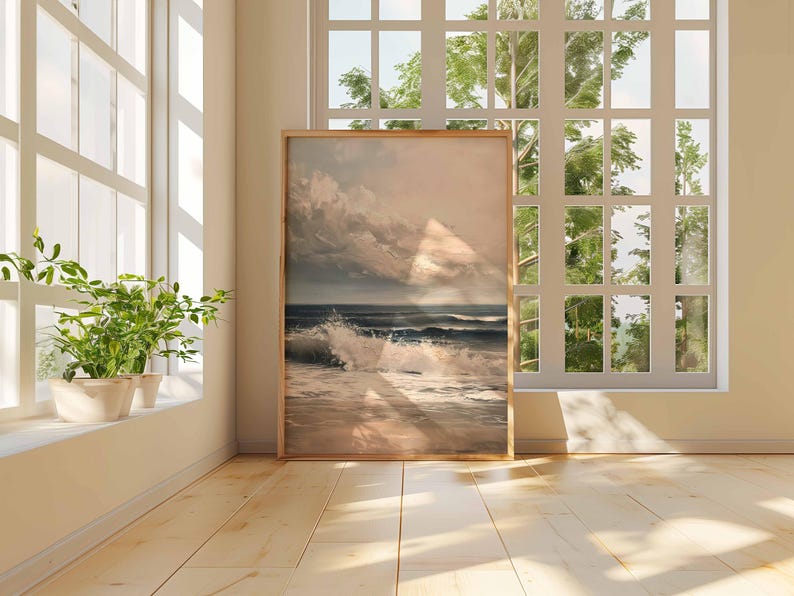 May include: A framed art print of a seascape with crashing waves and a cloudy sky. The artwork is displayed in a room with a large window and natural light. The frame is a light brown color.