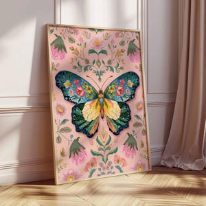 May include: A framed art print featuring a colorful butterfly with floral patterns. The butterfly has blue, yellow, and green wings with red and yellow flower details. The background is a soft pink with floral and leaf designs. The frame is a light wood color.