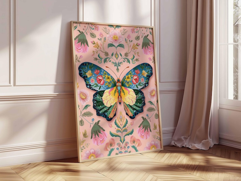 May include: A framed art print featuring a colorful butterfly with floral patterns. The butterfly has blue, yellow, and green wings with red and yellow flower details. The background is a soft pink with floral and leaf designs. The frame is a light wood color.