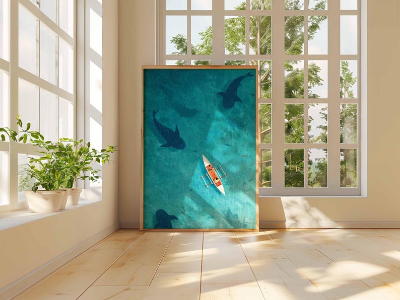 May include: A framed art print depicts an aerial view of a turquoise ocean with dark blue silhouettes of marine life. A white and orange canoe is in the center. The artwork is displayed in a bright room with a window.