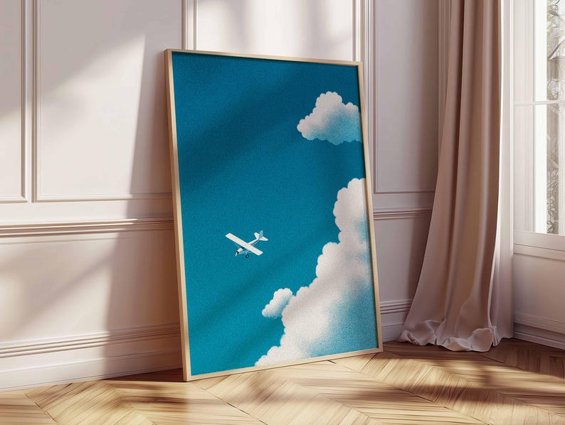 Peut inclure: Une affiche encadr&eacute;e repr&eacute;sentant un ciel bleu avec des nuages blancs et un petit avion blanc. L'&oelig;uvre d'art a un cadre en bois clair et est appuy&eacute;e contre un mur blanc et un sol en bois.
