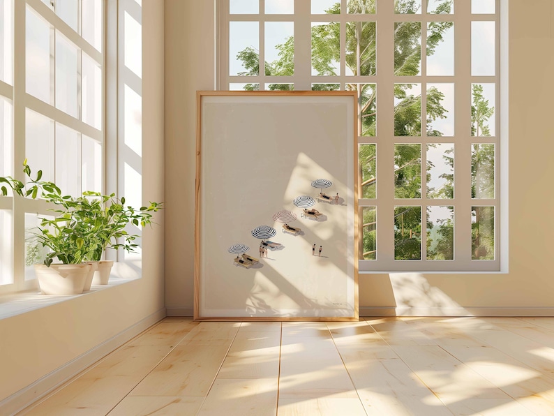 May include: A framed art print showing a beach scene with figures under striped umbrellas. The artwork is displayed in a room with a large window, letting in natural light. The print has a light wood frame.