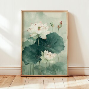Puede incluir: Una impresi&oacute;n art&iacute;stica enmarcada que presenta una pintura de acuarela de flores de loto blancas con hojas verdes. La obra de arte tiene una paleta de colores suaves y apagados con tonos de verde, blanco y rosa. La pintura se muestra en un marco de madera.