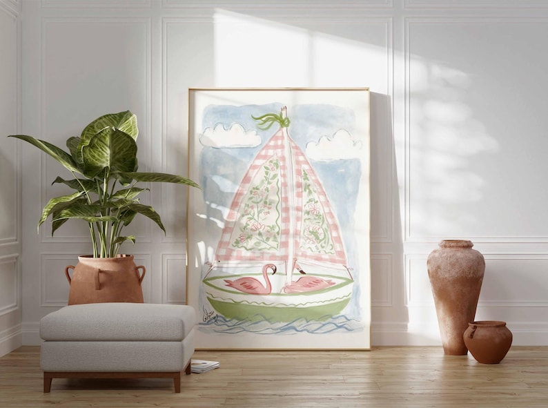 May include: Watercolor painting of a sailboat with a pink and white checkered sail, floral details, and two pink flamingos. The artwork is framed and leans against a white wall. A large potted plant, a gray ottoman, and terracotta vases are in the foreground.