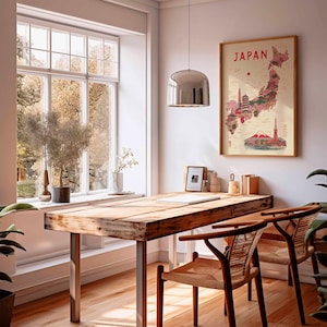 May include: A wooden desk with metal legs and two woven chairs sits in front of a large window. A framed map of Japan hangs on the wall. A silver pendant light hangs above the desk. The map is in a wooden frame and features a red and pink illustration of Japan.