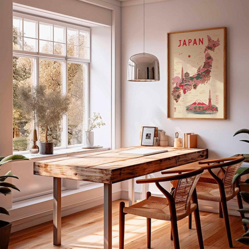 May include: A wooden desk with metal legs and two woven chairs sits in front of a large window. A framed map of Japan hangs on the wall. A silver pendant light hangs above the desk. The map is in a wooden frame and features a red and pink illustration of Japan.