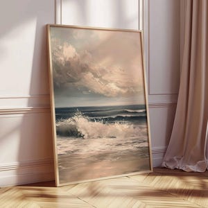 May include: A framed art print depicting a seascape with crashing waves and a dramatic sky. The artwork features a palette of blues, whites, and muted pinks, creating a serene yet powerful coastal scene. The frame is a light wood color.