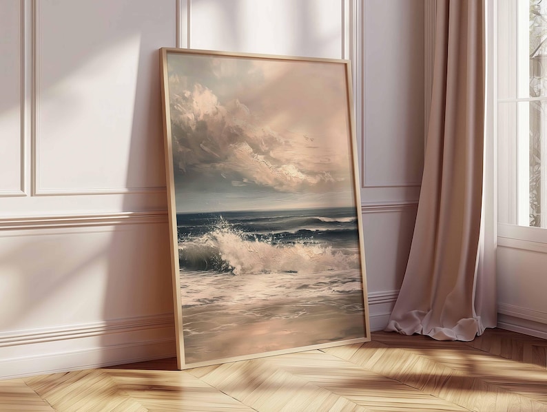 May include: A framed art print depicting a seascape with crashing waves and a dramatic sky. The artwork features a palette of blues, whites, and muted pinks, creating a serene yet powerful coastal scene. The frame is a light wood color.