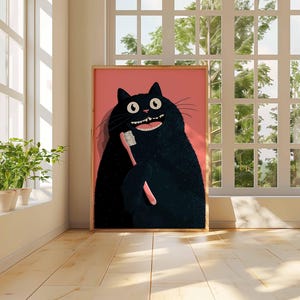 Op de afbeelding: Een ingelijste kunstdruk met een cartoon zwarte kat die een roze tandenborstel vasthoudt. De kat heeft een brede, tandige grijns en grote, ronde ogen. De achtergrond is effen roze. Het kunstwerk wordt getoond in een kamer met een raam en houten vloeren.