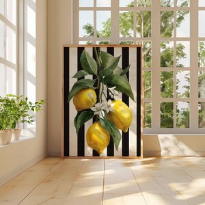 May include: A framed art print featuring a lemon branch with three yellow lemons, green leaves, and white blossoms against a black and white striped background. The artwork is displayed in a room with a window and potted plants.