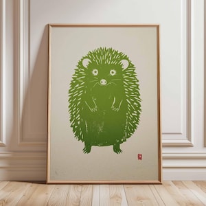 Pu&ograve; includere: Una stampa incorniciata con un'illustrazione di un riccio verde. Il riccio &egrave; raffigurato in uno stile linoleografico stilizzato con un aspetto strutturato. L'opera d'arte &egrave; ambientata su uno sfondo neutro e incorniciata in legno chiaro.