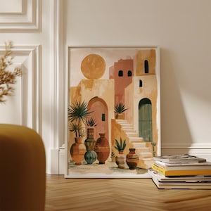 Peut inclure: Une impression d'art encadr&eacute;e repr&eacute;sentant une sc&egrave;ne de d&eacute;sert avec des b&acirc;timents aux tons p&ecirc;che, beige et marron. L'&oelig;uvre pr&eacute;sente un grand soleil, des escaliers, des arches et des vases d&eacute;coratifs avec des plantes. L'impression est expos&eacute;e sur un sol en bois.