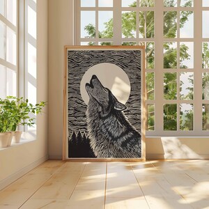 May include: A black and white print of a wolf howling at the moon, framed in wood. The artwork is set in a room with a large window, allowing natural light to illuminate the scene. The print is leaning against a wall.