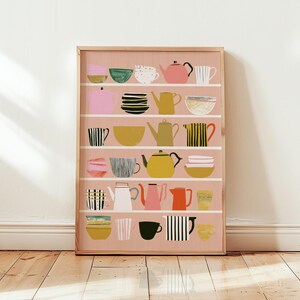 Puede incluir: Una lámina de arte mural rectangular con fondo rosa y cinco estantes blancos horizontales. Los estantes muestran una colección de teteras, tazas y cuencos ilustrados en varios colores, incluyendo amarillo, negro, blanco, rojo y verde.