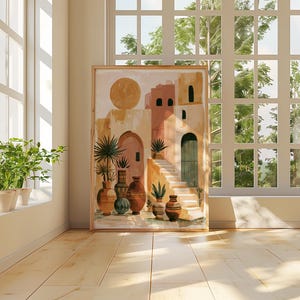 Peut inclure: Une impression d'art encadr&eacute;e repr&eacute;sentant une sc&egrave;ne de village d&eacute;sertique avec un grand soleil, des b&acirc;timents en terre cuite et divers vases. L'&oelig;uvre est expos&eacute;e dans une pi&egrave;ce lumineuse avec une fen&ecirc;tre et des plantes en pot.