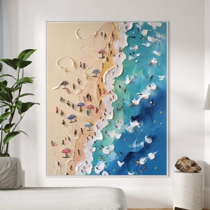 May include: A framed painting of a beach scene. The artwork shows a sandy beach with people and colourful umbrellas, leading to turquoise and deep blue ocean waves. The painting has a textured, three-dimensional effect.
