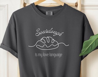 May include: A dark gray t-shirt with a white graphic design that says "Sourdough is my love language" and a simple line drawing of a loaf of bread.