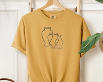 May include: A mustard yellow t-shirt with a graphic of three stylized vases and the text "Pot Dealer."