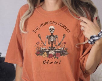 May include: Orange t-shirt with a skeleton meditating with flowers and the text "The Horrors Persist But So Do I"