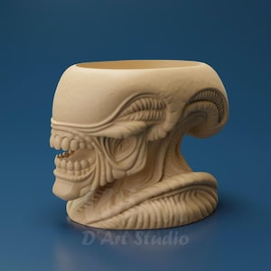 May include: A beige, sculpted Alien head-shaped planter. The detailed design features the creature's iconic elongated skull, open mouth with teeth, and textured facial features. The planter has a wide opening at the top and the text "D'Art Studio" at the bottom.