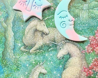 Op de afbeelding: Een paar handgemaakte oorbellen met een blauwe en roze ster en een halve maan met een slapend gezichtontwerp. De oorbellen zijn gemaakt van polymer clay en hebben gouden kettingschakels.