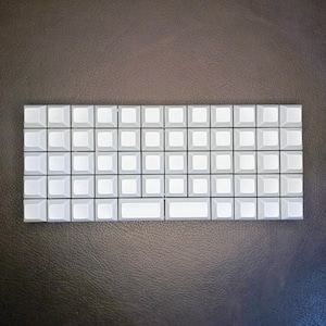 May include: A white mechanical keyboard with a blank keycap layout. The keyboard has a total of 60 keys.