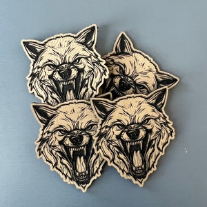 Pode incluir: Quatro adesivos de papel castanho com ilustra&ccedil;&otilde;es de tinta preta de um rosto de lobo que rosna com a boca aberta.