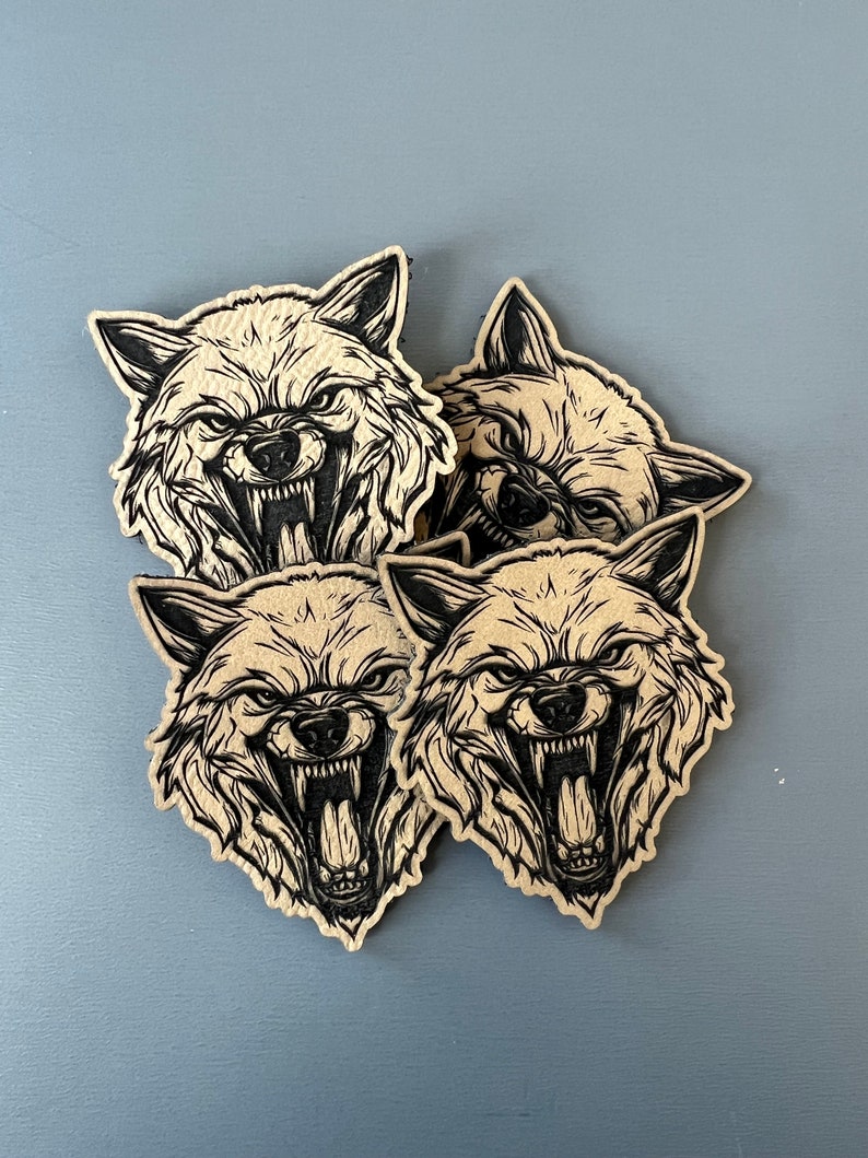 Pode incluir: Quatro adesivos de papel castanho com ilustra&ccedil;&otilde;es de tinta preta de um rosto de lobo que rosna com a boca aberta.