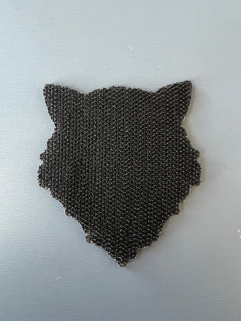 Pode incluir: Etiqueta preta de velcro em forma de cabe&ccedil;a de lobo.