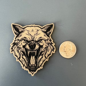 Pode incluir: Um recorte de madeira de uma cabe&ccedil;a de lobo com uma express&atilde;o de rosnado. O lobo &eacute; retratado em preto e branco, com um design detalhado.