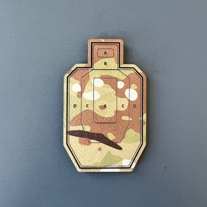 May include: A camouflage-patterned target with a black outline and letters A, B, C, and D printed on it.