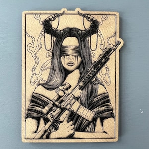 May include: A black and white illustration of a woman with horns and blindfolded eyes holding a rifle. The background is a light brown colour with a swirling pattern.