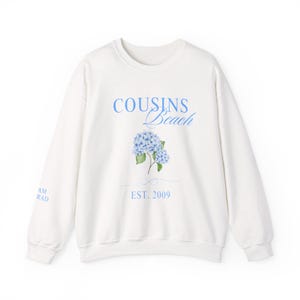 Peut inclure: Sweat-shirt blanc avec un motif floral bleu et le texte "COUSINS Beach EST. 2009" imprimé sur le devant.