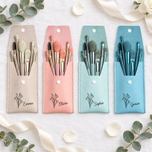 Op de afbeelding: Vier rechthoekige make-up kwastenetuis in beige, roze, lichtgroen en blauw, elk met een drukknoopsluiting. Elk etui bevat vijf kwasten en is voorzien van een zwarte florale lijntekening met de namen Emma, Olivia, Sophie en Grace erop gedrukt.
