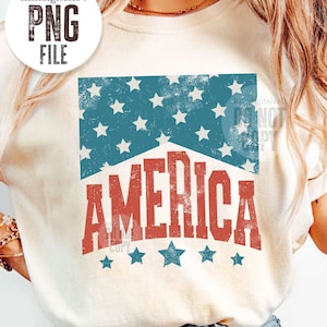 May include: Cream-colored t-shirt with a distressed graphic featuring the word "AMERICA" in red, beneath a blue section with white stars. The shirt is paired with blue denim jeans. The image includes the text "PNG FILE".