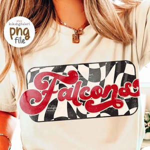 May include: Cream-colored t-shirt with a red and black checkered design and the word "Falcons" in a retro script. The person is wearing a gold necklace and bracelets, and checkered shorts.
