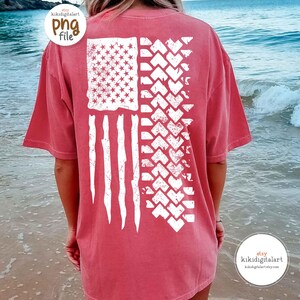 May include: A red-orange t-shirt with a distressed white American flag design. The flag features stars, stripes, and a tire track pattern. The shirt is a comfortable, casual style.
