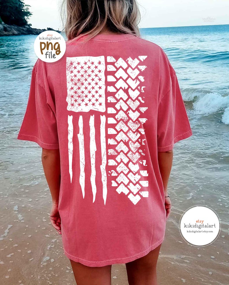 May include: A red-orange t-shirt with a distressed white American flag design. The flag features stars, stripes, and a tire track pattern. The shirt is a comfortable, casual style.