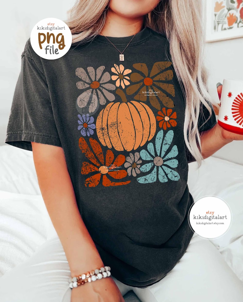 Op de afbeelding: Donkergrijs t-shirt met een pompoen- en bloemenontwerp in oranje, bruin, blauw en grijs. Het shirt heeft een vintage, distressed look. De Etsy shopnaam "kikidigitalart" is zichtbaar op het shirt.