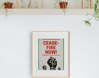 May include: A framed poster with a white background and green border. The poster features a black fist with a peace sign in the palm and the text "CEASE-FIRE NOW!" in red.