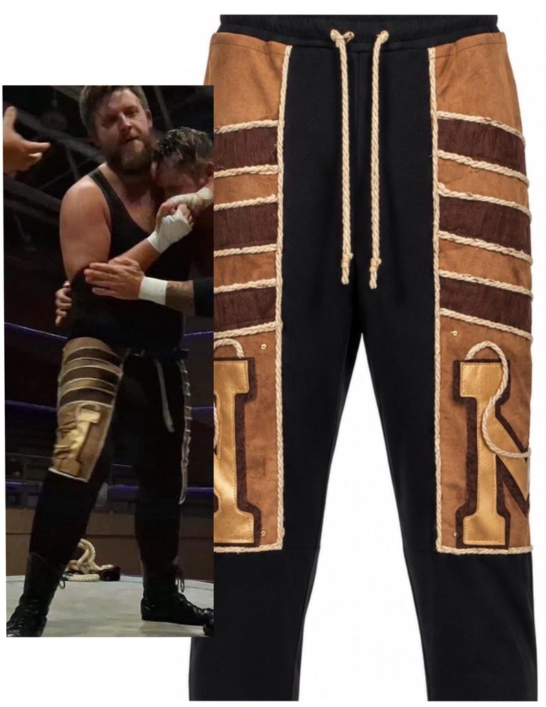 May include: Black sweatpants featuring tan suede-like side panels with horizontal dark brown textured stripes and thick cream-colored rope detailing. The pants include a matching cream drawstring at the waist and large gold-colored letter patches.
