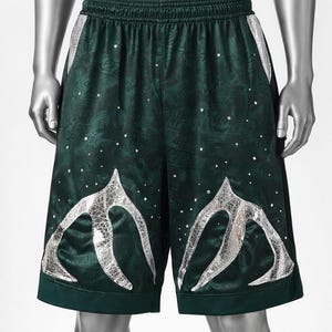May include: Dark green athletic shorts featuring an elastic waistband, a subtle tonal pattern throughout the fabric, scattered small clear rhinestones, and two large, silver, cracked-texture graphic appliques on the lower front panels.