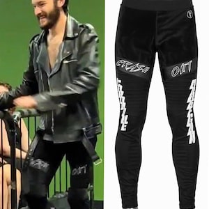 May include: Black pants featuring a wide waistband, ribbed knee panels, and white graphic text on the thighs reading CRASH OUT. The design includes additional white vertical text along the lower legs and a small circular logo on the upper hip.