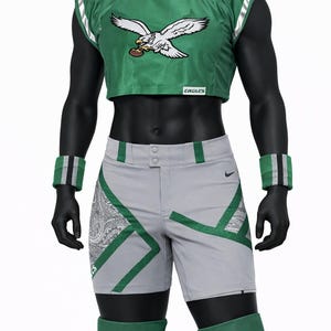 May include: A green cropped jersey with an eagle graphic and the text EAGLES, paired with grey athletic shorts featuring green and paisley accents. The outfit includes green wristbands and green knee pads with the text EAGLES printed on them.